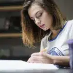 A focused student writes notes while studying for the International Biology Olympiad.