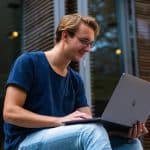 A student sits outside using a laptop to research whether Colgate is an Ivy League school.