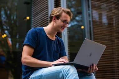 A student sits outside using a laptop to research whether Colgate is an Ivy League school.