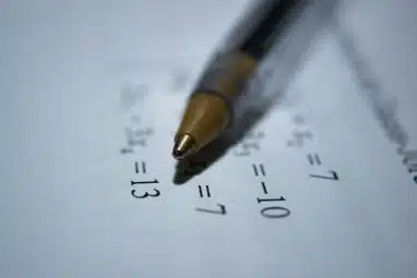 Close-up of a pen resting on a sheet of math equations, representing preparation and problem-solving for the ARML competition.