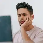 A young man looks thoughtfully at his laptop while researching what is the highest GPA.