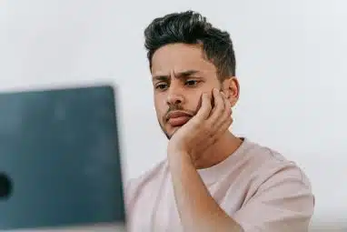A young man looks thoughtfully at his laptop while researching what is the highest GPA.