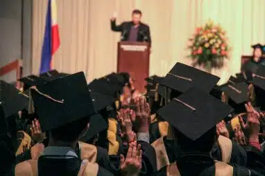 Graduates raising their hands during a commencement ceremony, symbolizing academic achievement and leadership tied to institutions often led by the highest paid university presidents.