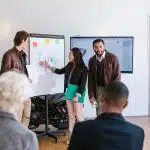 A group of LaunchX students present their startup ideas using charts and sketches on a whiteboard during a workshop session.