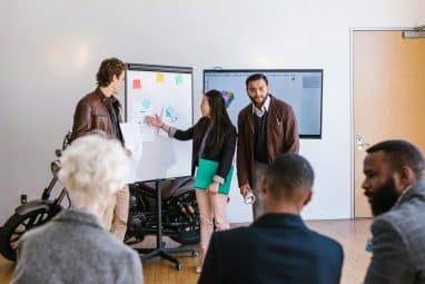 A group of LaunchX students present their startup ideas using charts and sketches on a whiteboard during a workshop session.