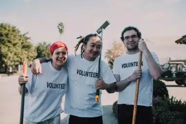 Three young Points of Light volunteers wearing white shirts holding cleaning materials