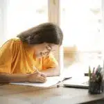 A high school student smiles while studying and writing notes for her high school classes.