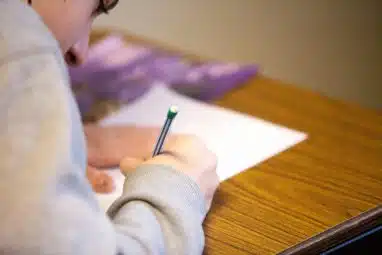 Student taking a written exam at a wooden desk, representing the testing process and preparation needed to meet Princeton SAT requirements.