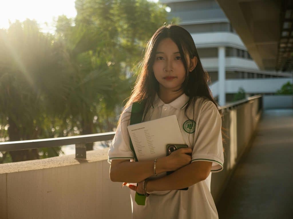 Student holding books while standing on a sunlit campus walkway, representing UIUC SAT requirements and preparation for competitive admission standards at the University of Illinois Urbana-Champaign.