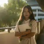 Student holding books while standing on a sunlit campus walkway, representing UIUC SAT requirements and preparation for competitive admission standards at the University of Illinois Urbana-Champaign.