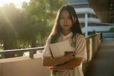 Student holding books while standing on a sunlit campus walkway, representing UIUC SAT requirements and preparation for competitive admission standards at the University of Illinois Urbana-Champaign.