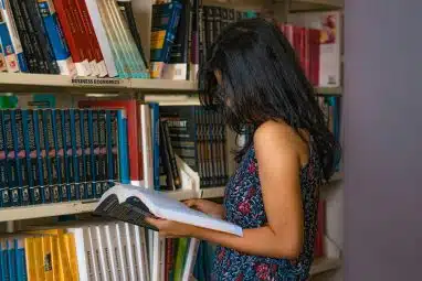 Student reading a textbook in a college library while researching direct admissions and understanding how the direct admissions process works for academic planning.