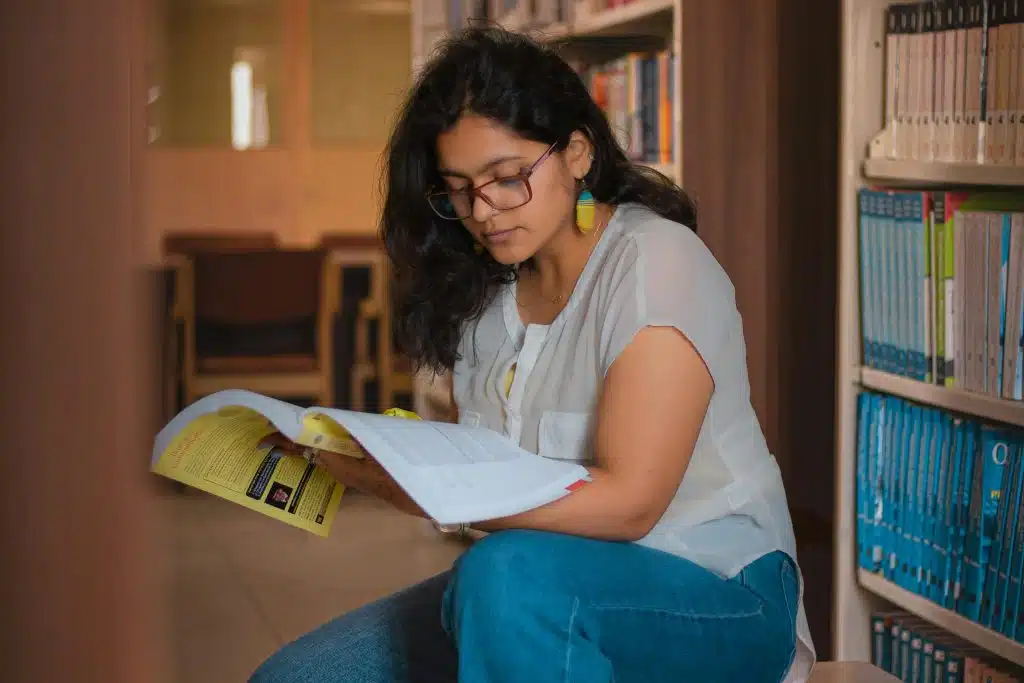 Student reading in a library while researching test optional colleges and planning college applications without SAT or ACT scores.