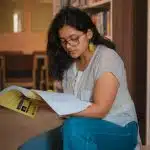 Student reading in a library while researching test optional colleges and planning college applications without SAT or ACT scores.
