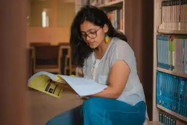 Student reading in a library while researching test optional colleges and planning college applications without SAT or ACT scores.