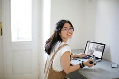 student in white smiling while working on the laptop for the claremont mckenna sat requirements