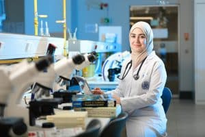 student sitting near a table with microscopes for the post bacc programs for medical school