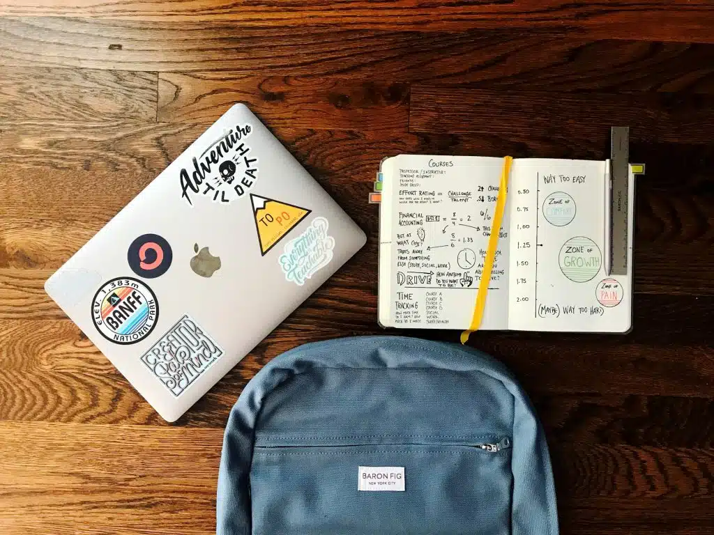 A flat overlay of laptop, open notebook, and a backpack of a student who asks"how many colleges should you apply to "