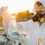 Student wearing protective gear collecting and testing a water sample outdoors for one of the top environmental science summer programs