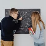 Two high school students solve equations on a chalkboard together, representing math competitions for high school students.