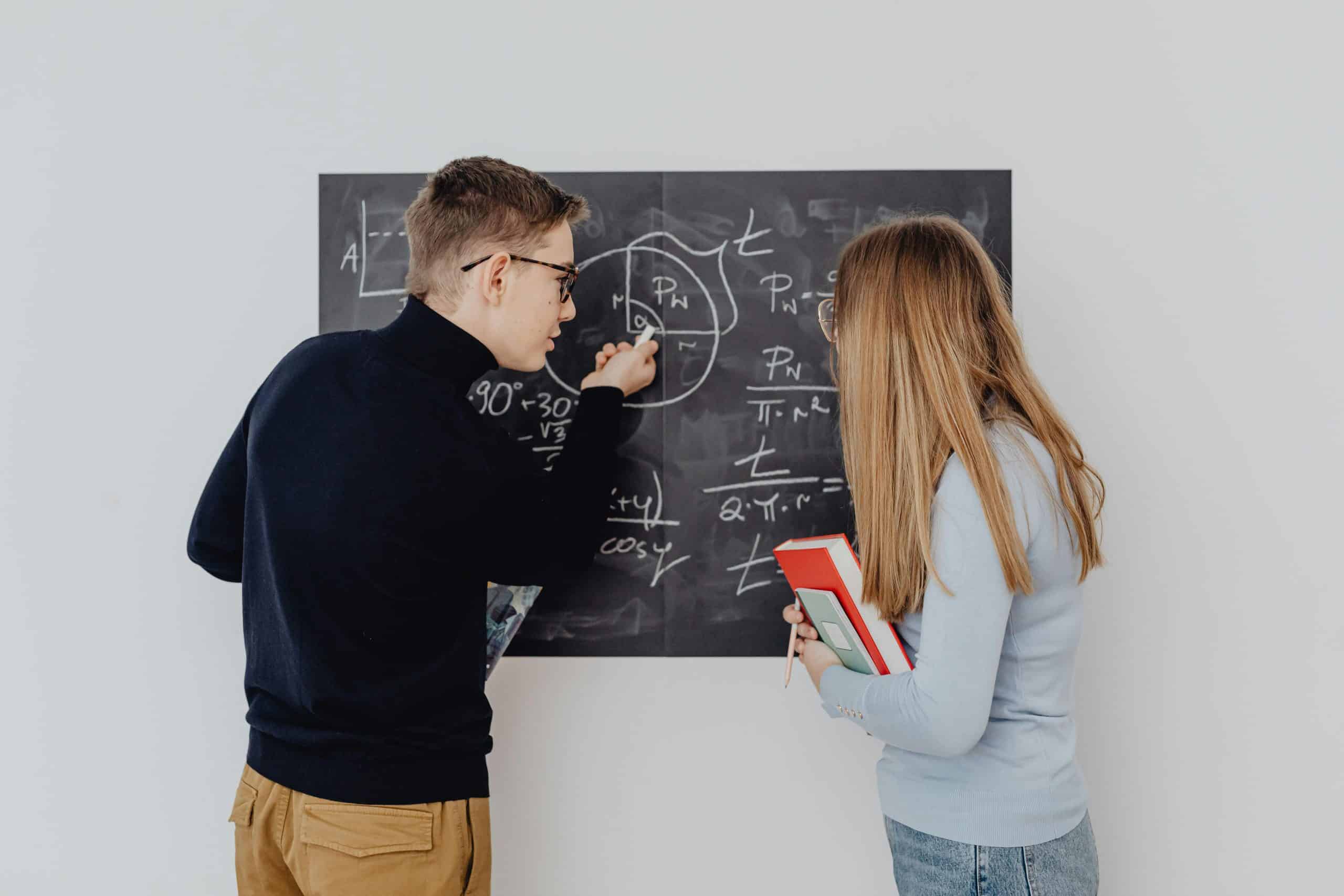 Two high school students solve equations on a chalkboard together, representing math competitions for high school students.
