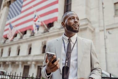 A professionally dressed individual standing outside a government building with an American flag, representing government internships for high school students.