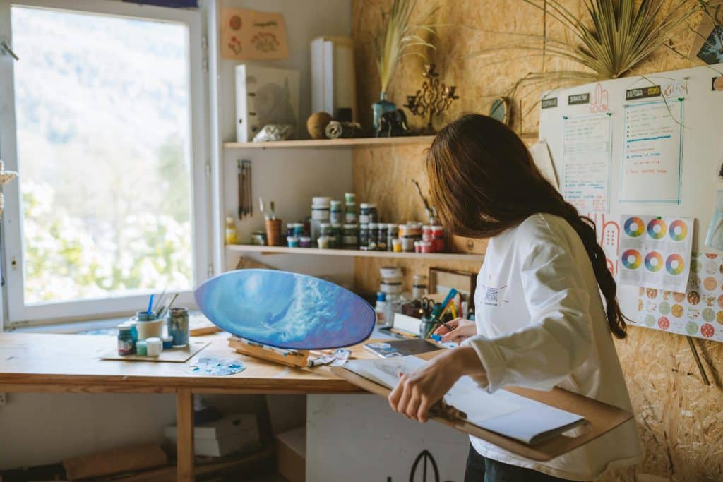 Student painting artwork in a studio for an Ocean Awareness Student Contest submission, with art supplies and canvas on a worktable