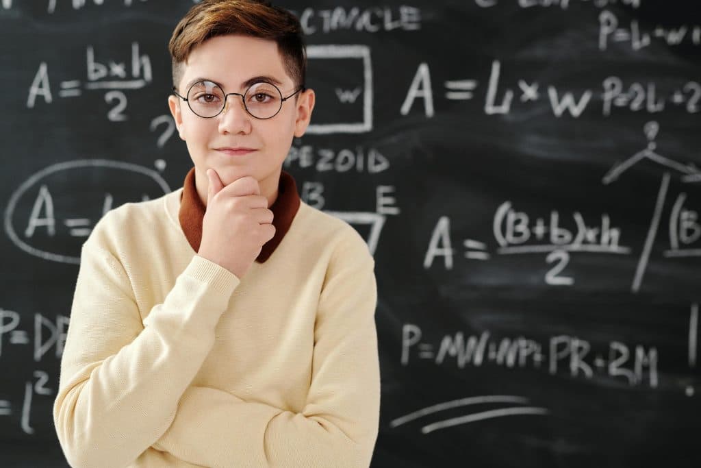 A student stands in front of a chalkboard with math formulas, symbolizing academic focus for Princeton vs Harvard.