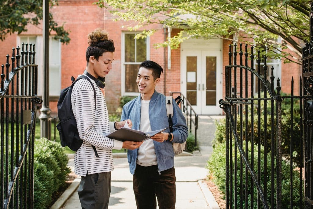 Two college students reviewing notes outside a campus building, representing a UC Berkeley vs MIT comparison in academic environment and student life