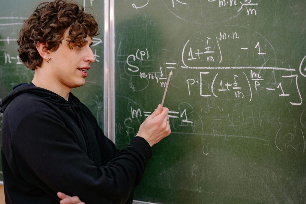 Curly-haired student pointing at complex math equations on a chalkboard at one of the best colleges for math