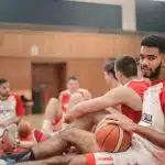 College basketball players sitting on a court during practice, representing student-athlete recruitment opportunities with NCSA