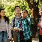Campus tour with diverse college students walking outdoors, one pointing ahead while holding a guidebook