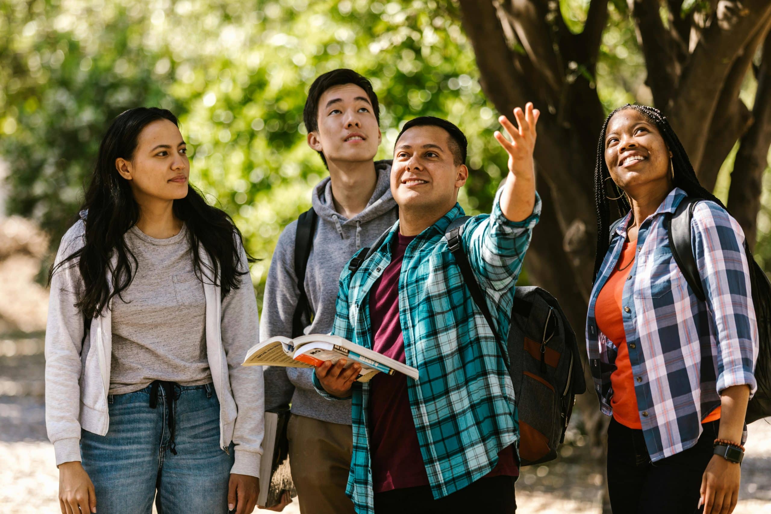 Campus tour with diverse college students walking outdoors, one pointing ahead while holding a guidebook