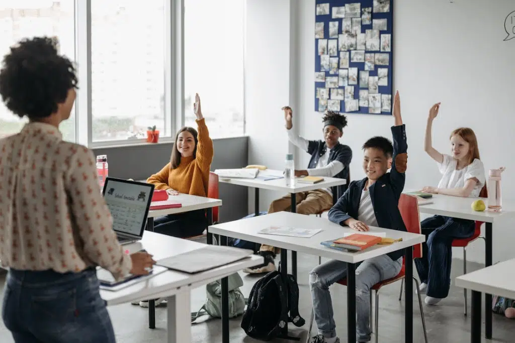 Teacher leading a classroom lesson as students raise their hands to participate, representing academic engagement and learning at some of the best high schools in America.