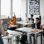 Teacher leading a classroom lesson as students raise their hands to participate, representing academic engagement and learning at some of the best high schools in America.