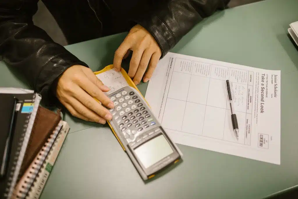 Student using a graphing calculator with a worksheet and notebooks on a desk to review FAFSA income limits
