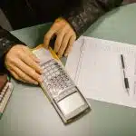Student using a graphing calculator with a worksheet and notebooks on a desk to review FAFSA income limits