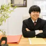 Yale admissions consultant in a dark suit smiling with arms crossed at a desk with a binder and folder